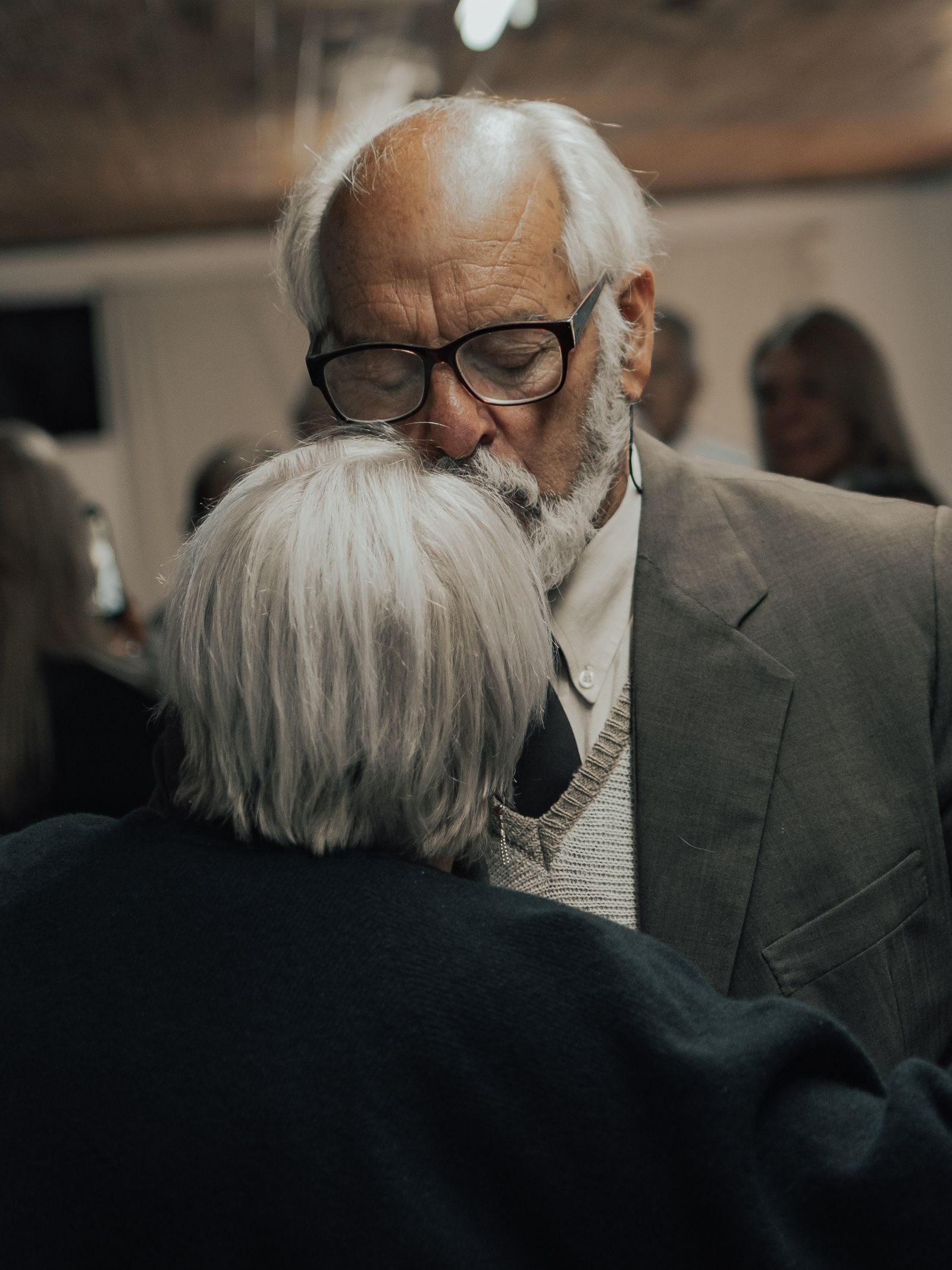 A senior couple sharing an emotional embrace at an indoor gathering.