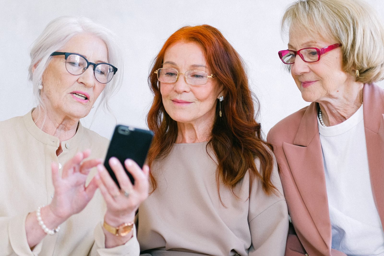 Cheerful senior women talking and using mobile phone while watching video online through internet together