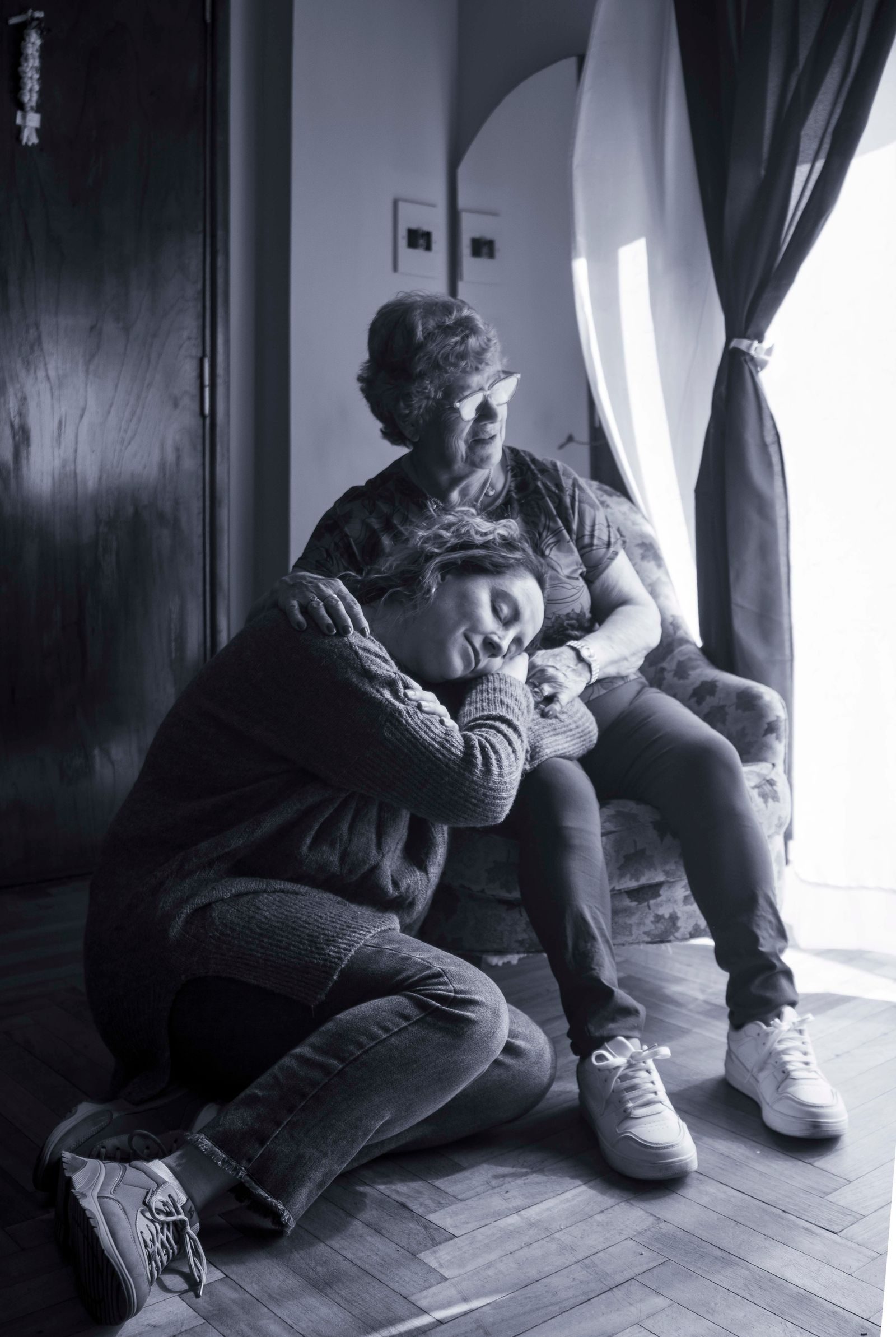 Touching scene of a woman resting her head on her elderly mother's knee, showcasing love and connection.