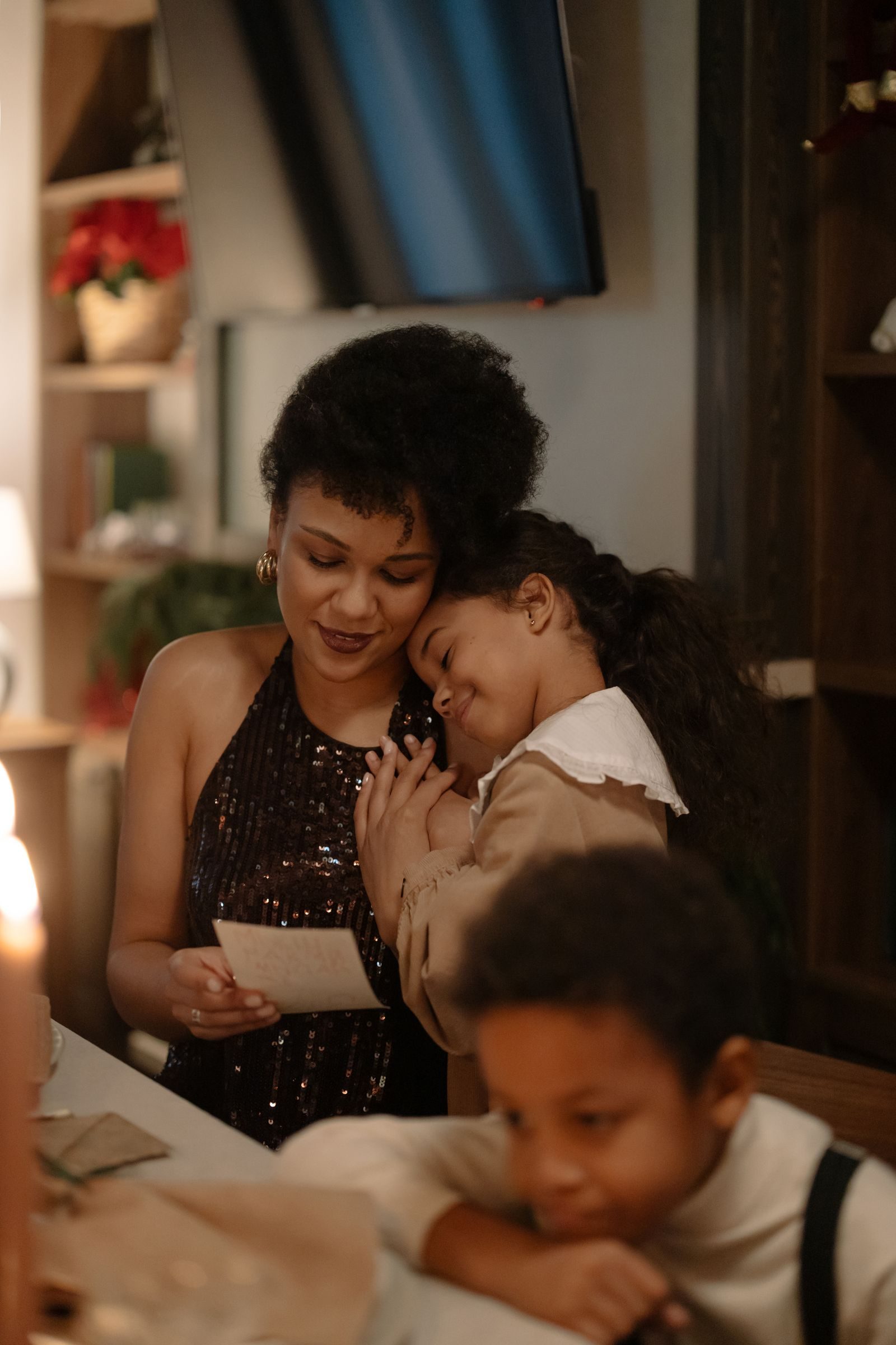 A mother and daughter share a loving hug at home during a festive holiday gathering.