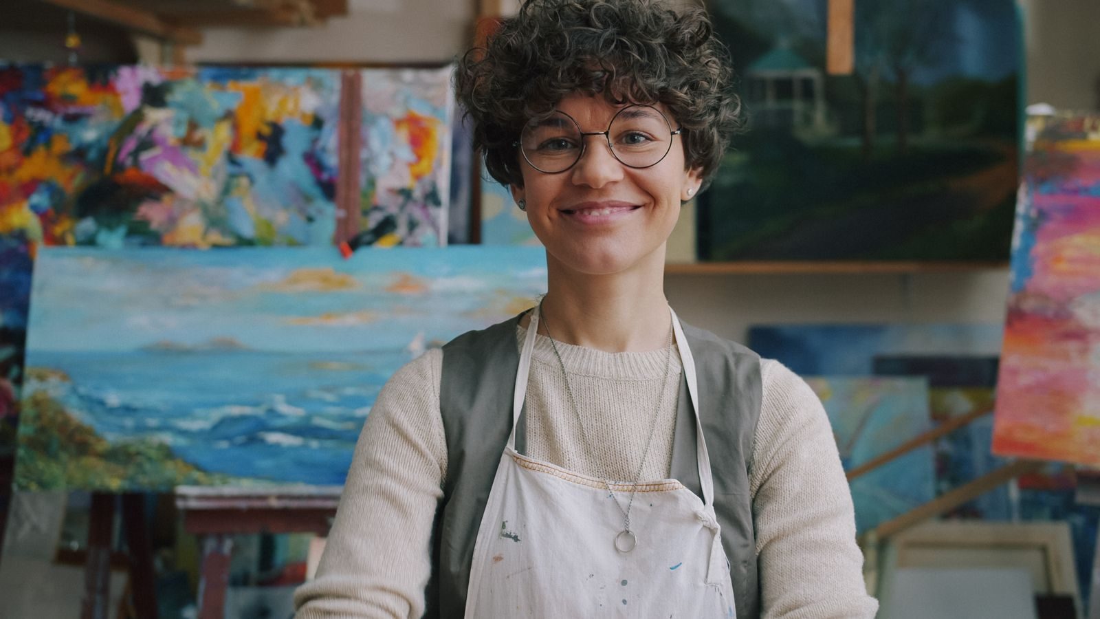 Artist in studio with vibrant paintings around, radiating creativity and joy.