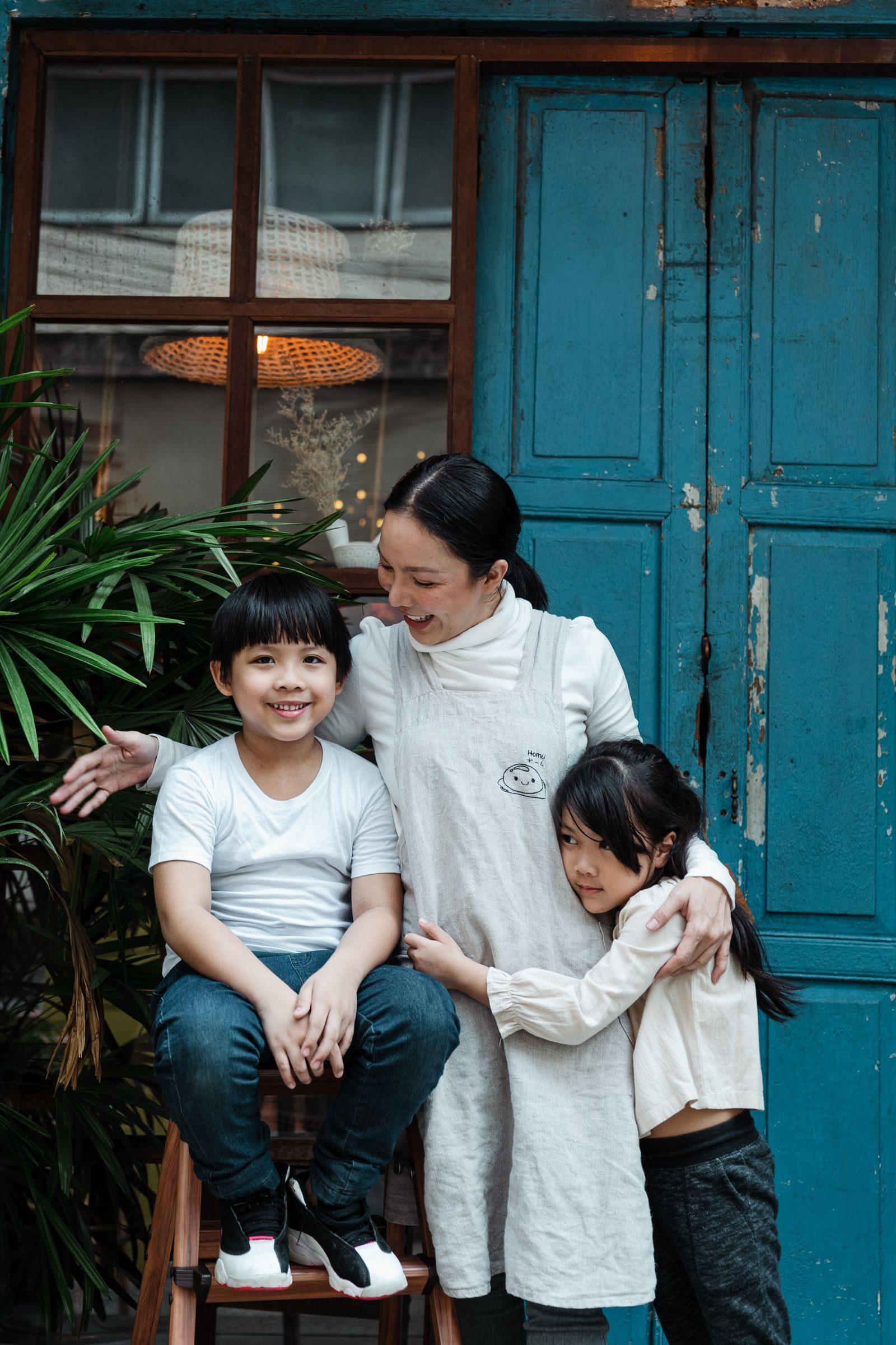 A joyful moment of a mother embracing her two children outside a rustic blue door.