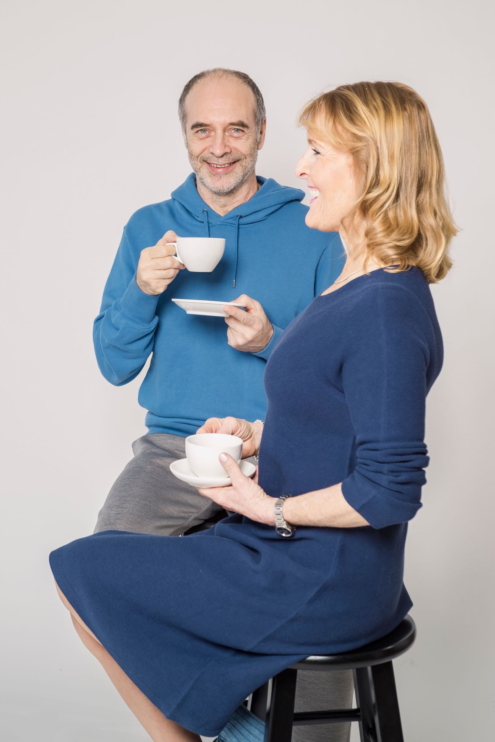 Smiling senior couple sitting indoors enjoying tea. Both appear happy and relaxed.