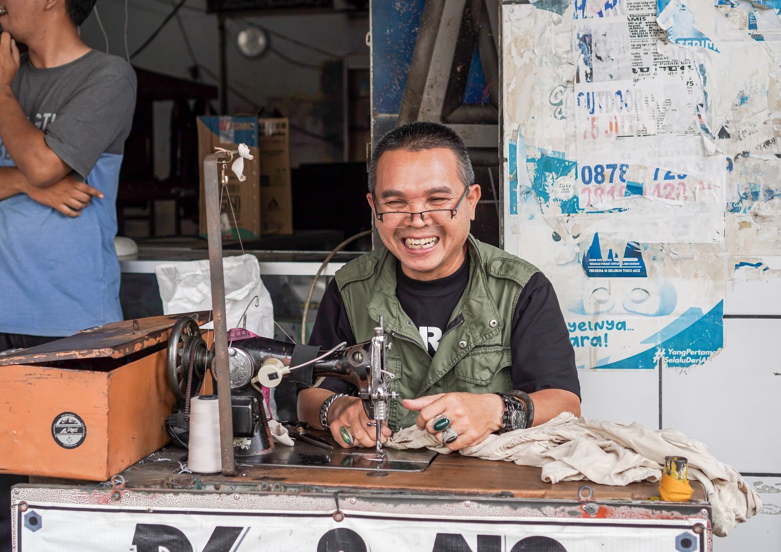 Smiling tailor working on vintage sewing machine in street market, capturing local craftsmanship and joy.