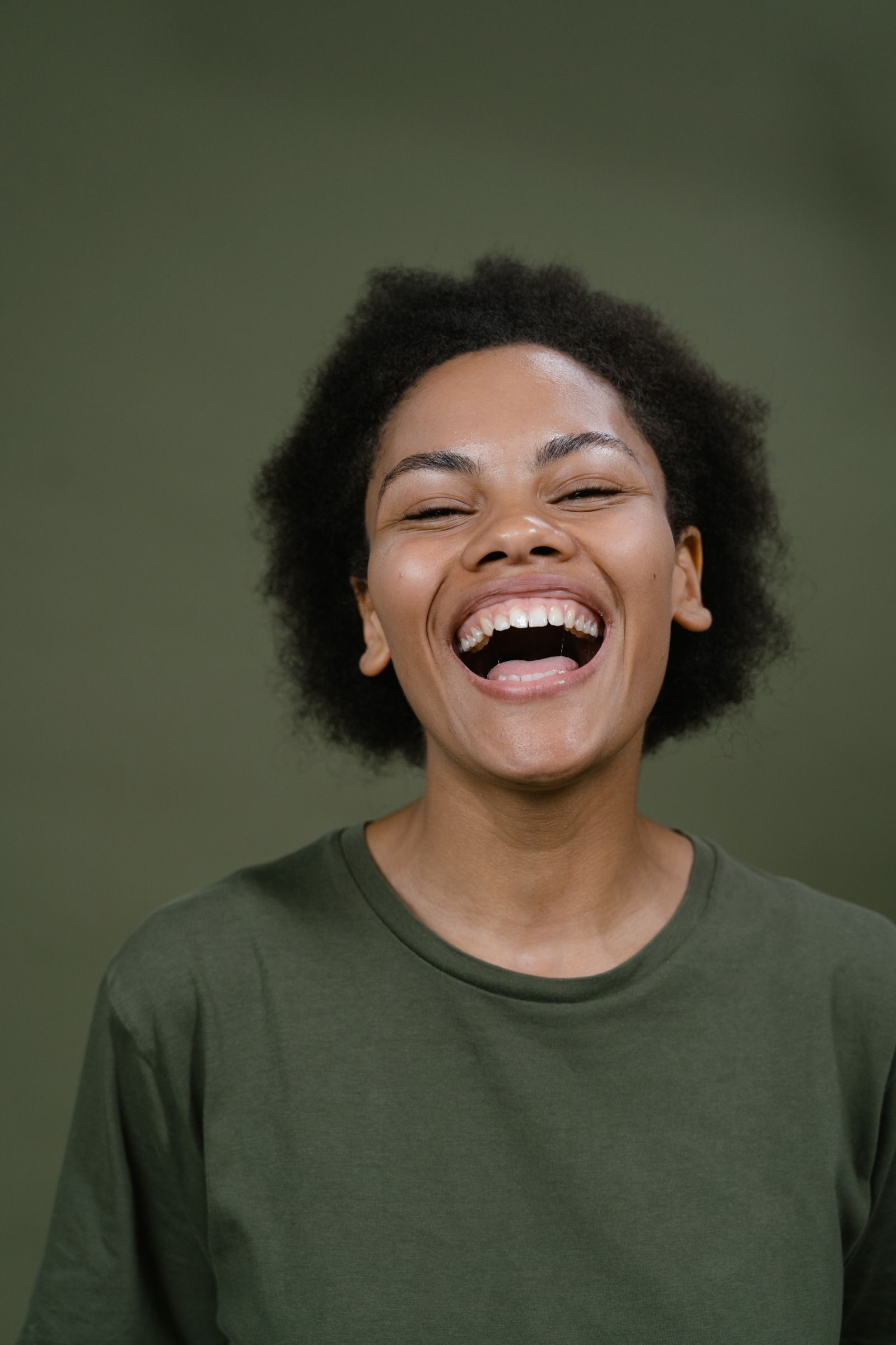 A vibrant woman laughing heartily in a studio with a green backdrop, exuding happiness.