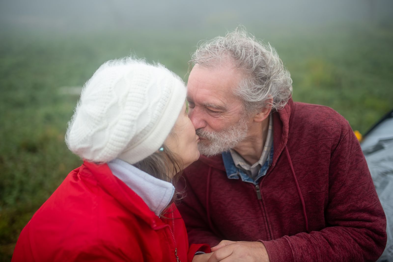 Senior couple sharing a loving kiss outdoors on a foggy day, capturing affection and connection.