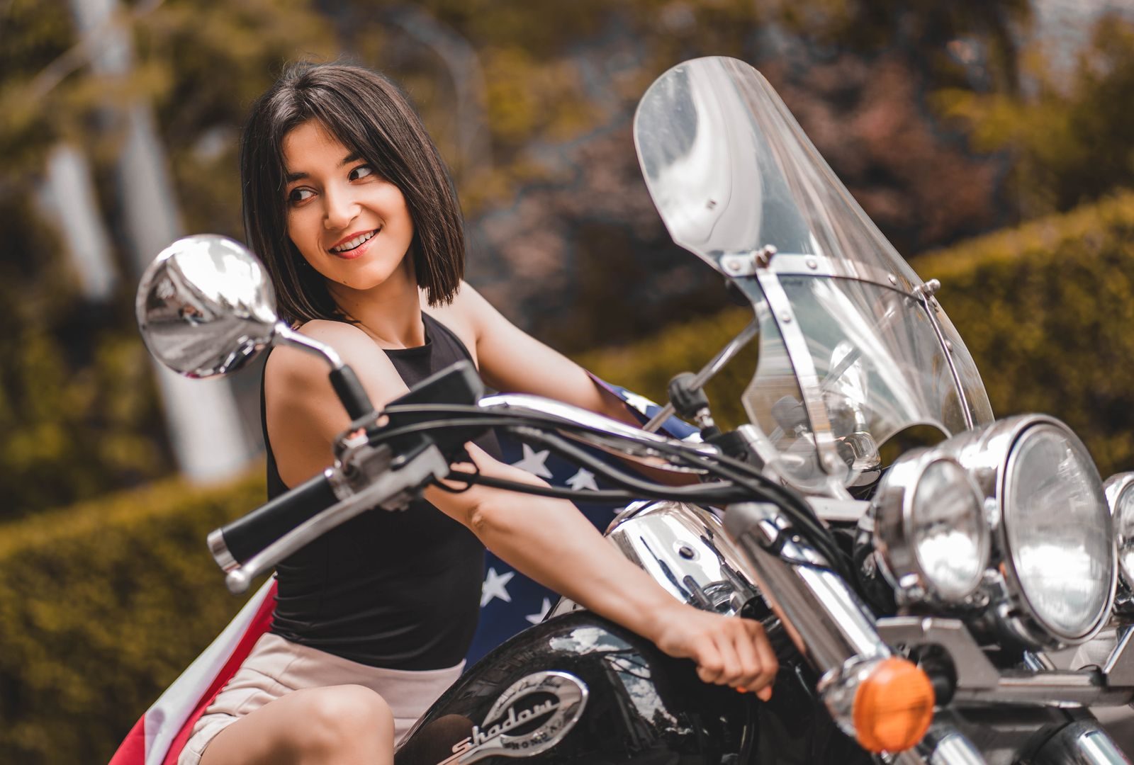 Cheerful woman with short brunette hair posing on a motorcycle outside.