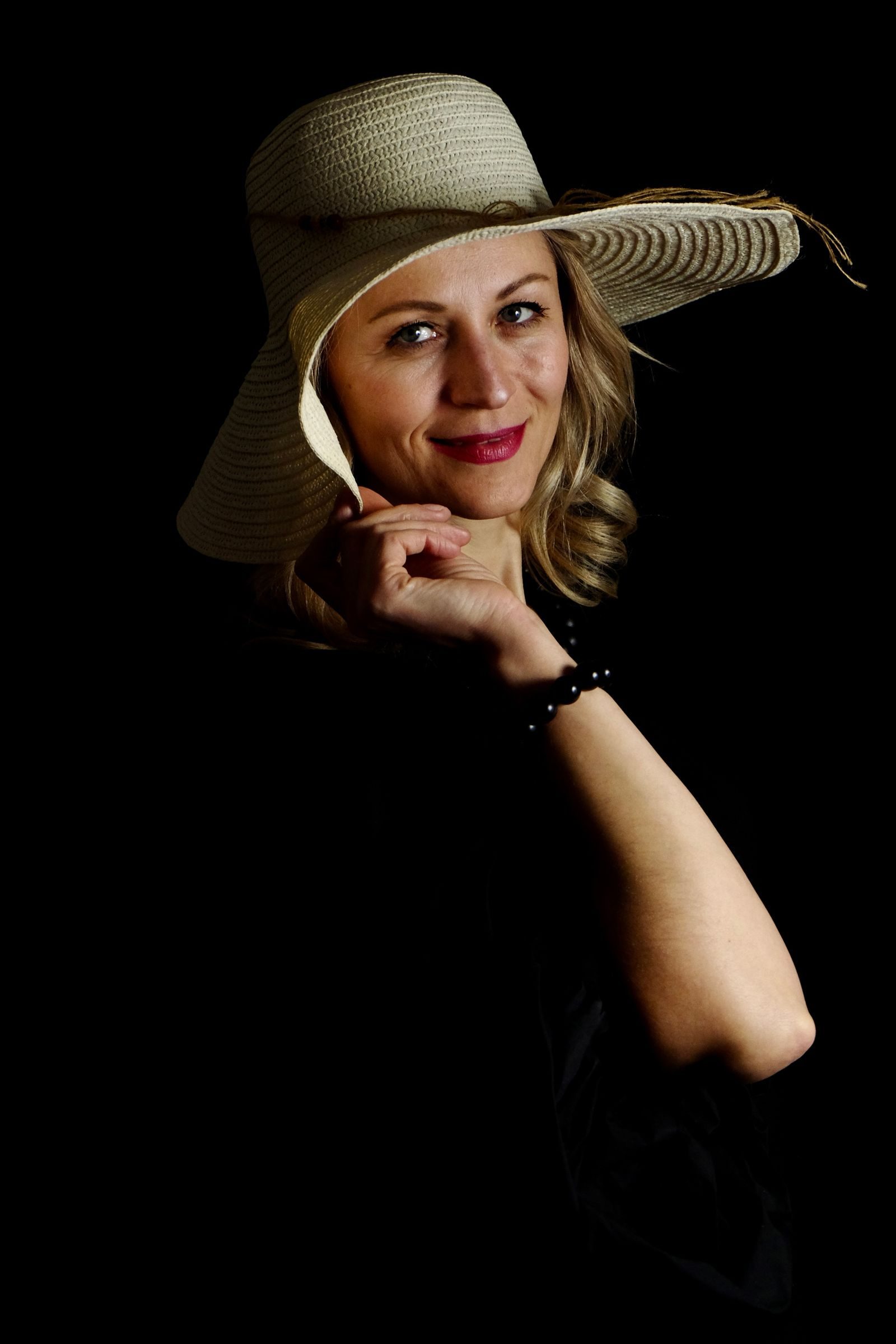 Chic portrait of a smiling woman in a stylish hat, with a black background, captured in studio.