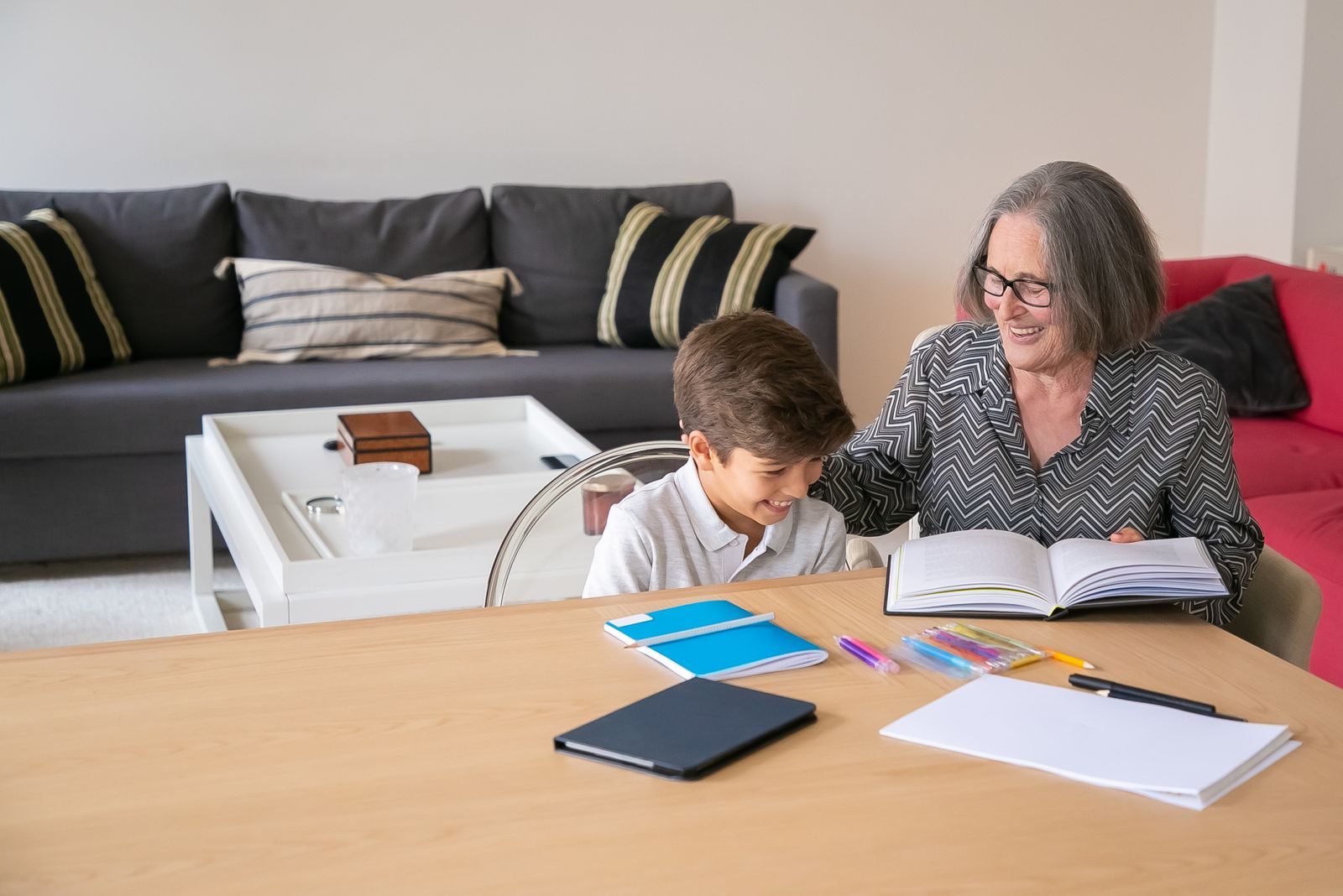 Elderly woman shares a happy reading moment with her young grandson at home, fostering warmth and bonding.