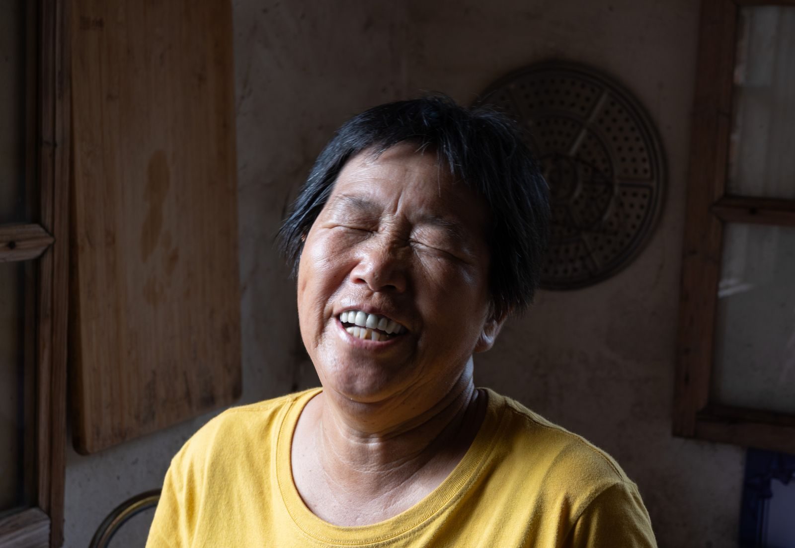 Elderly woman laughing joyfully, captured indoors in warm light.
