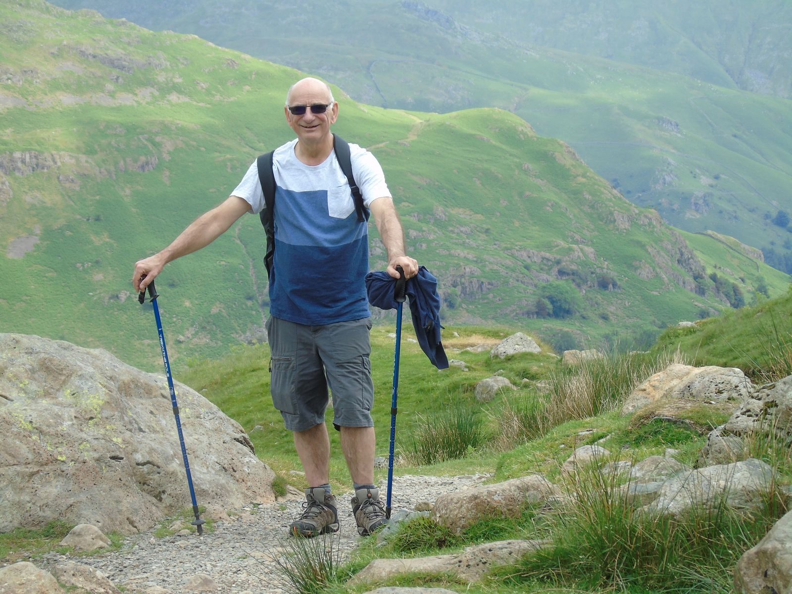 Elderly man hiking in the English mountains with trekking poles on a sunny day.