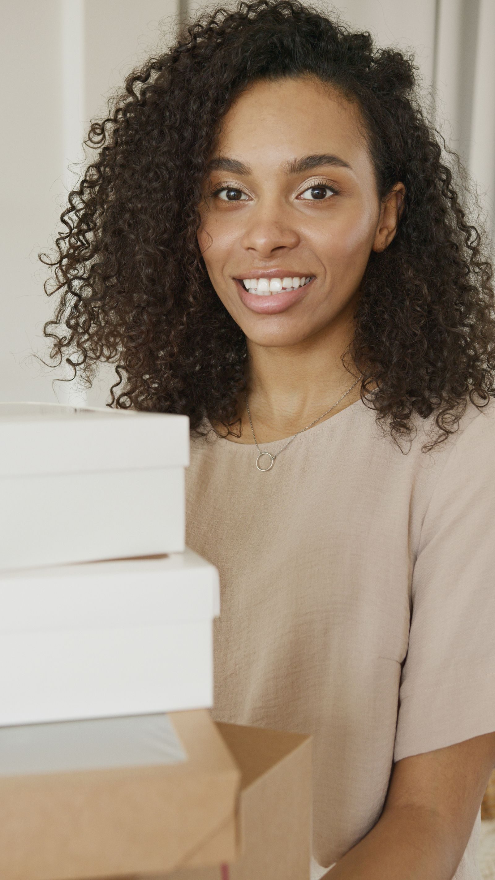 Confident woman with curly hair smiling amidst packages, symbolizing entrepreneurial success.