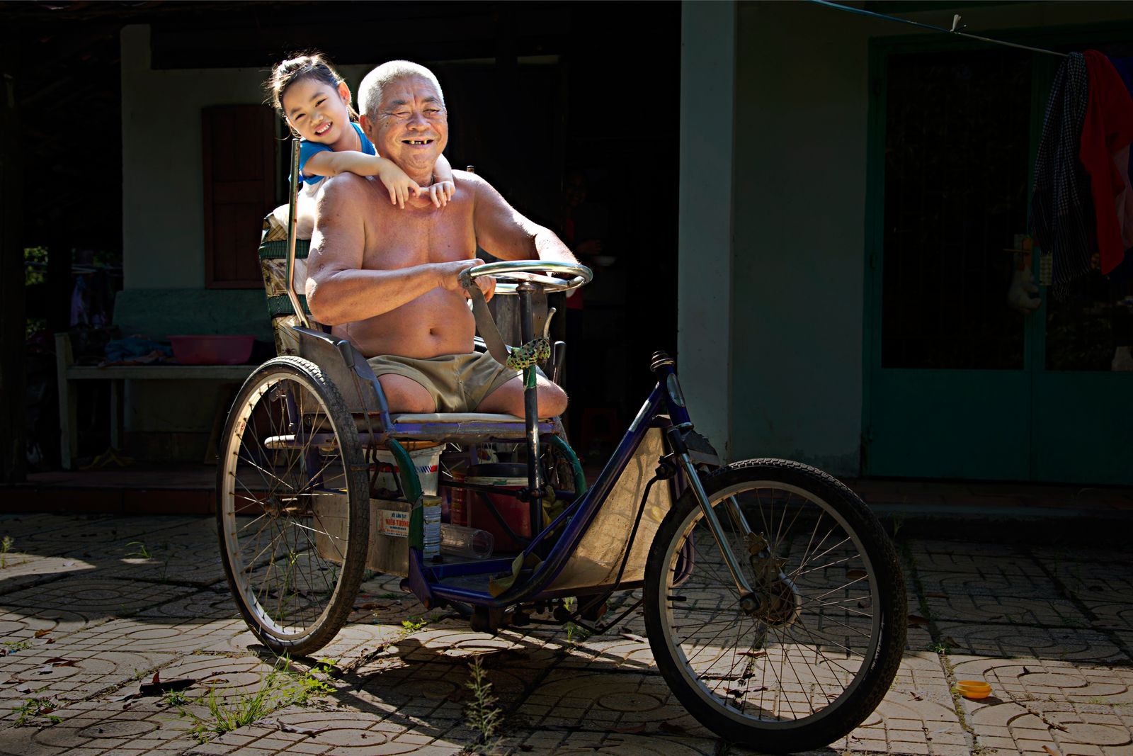 Elderly man and cheerful child enjoying a tricycle ride outdoors in sunlight.