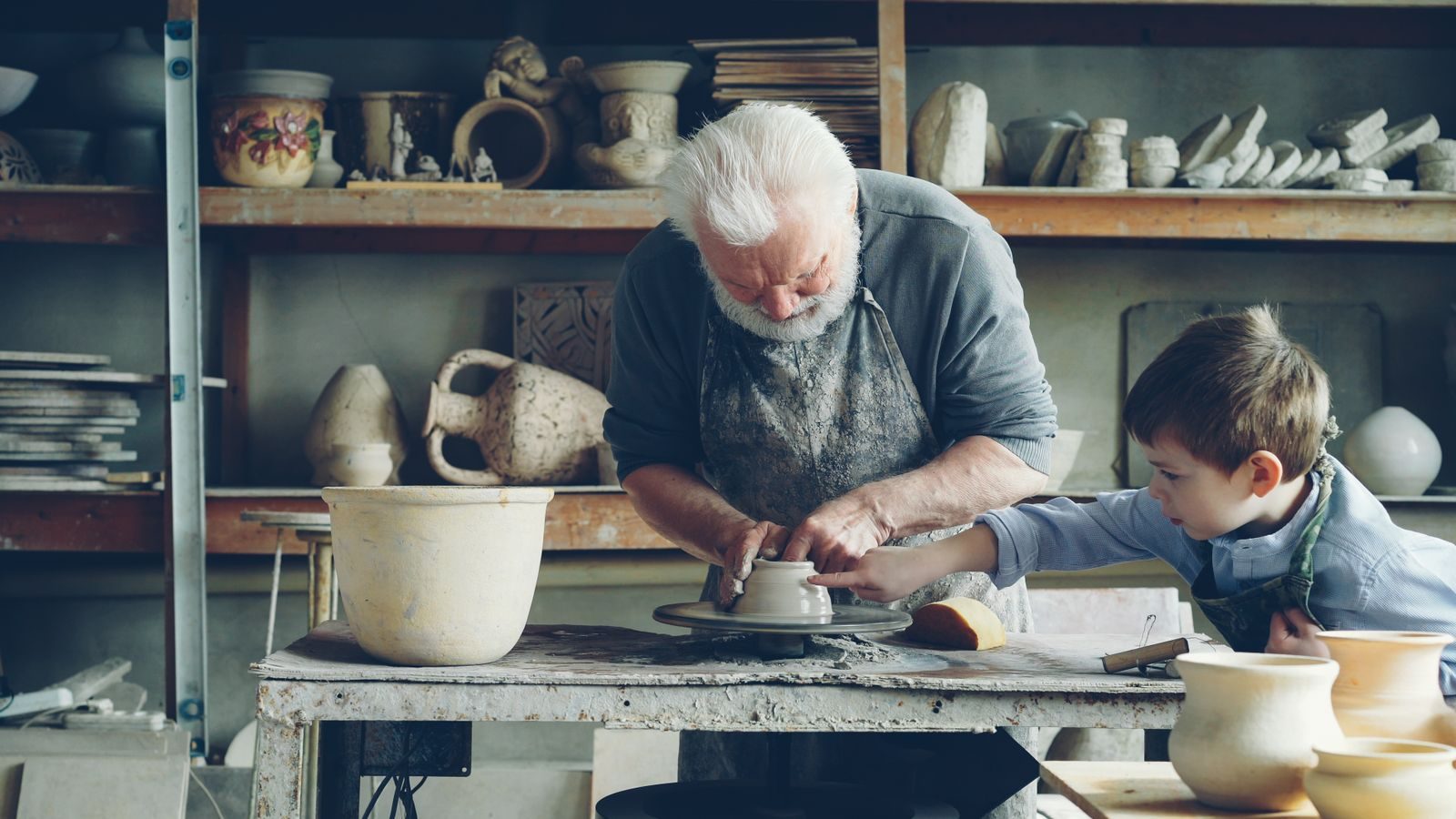 An elderly man and a child working together on clay pottery in an artisan workshop.