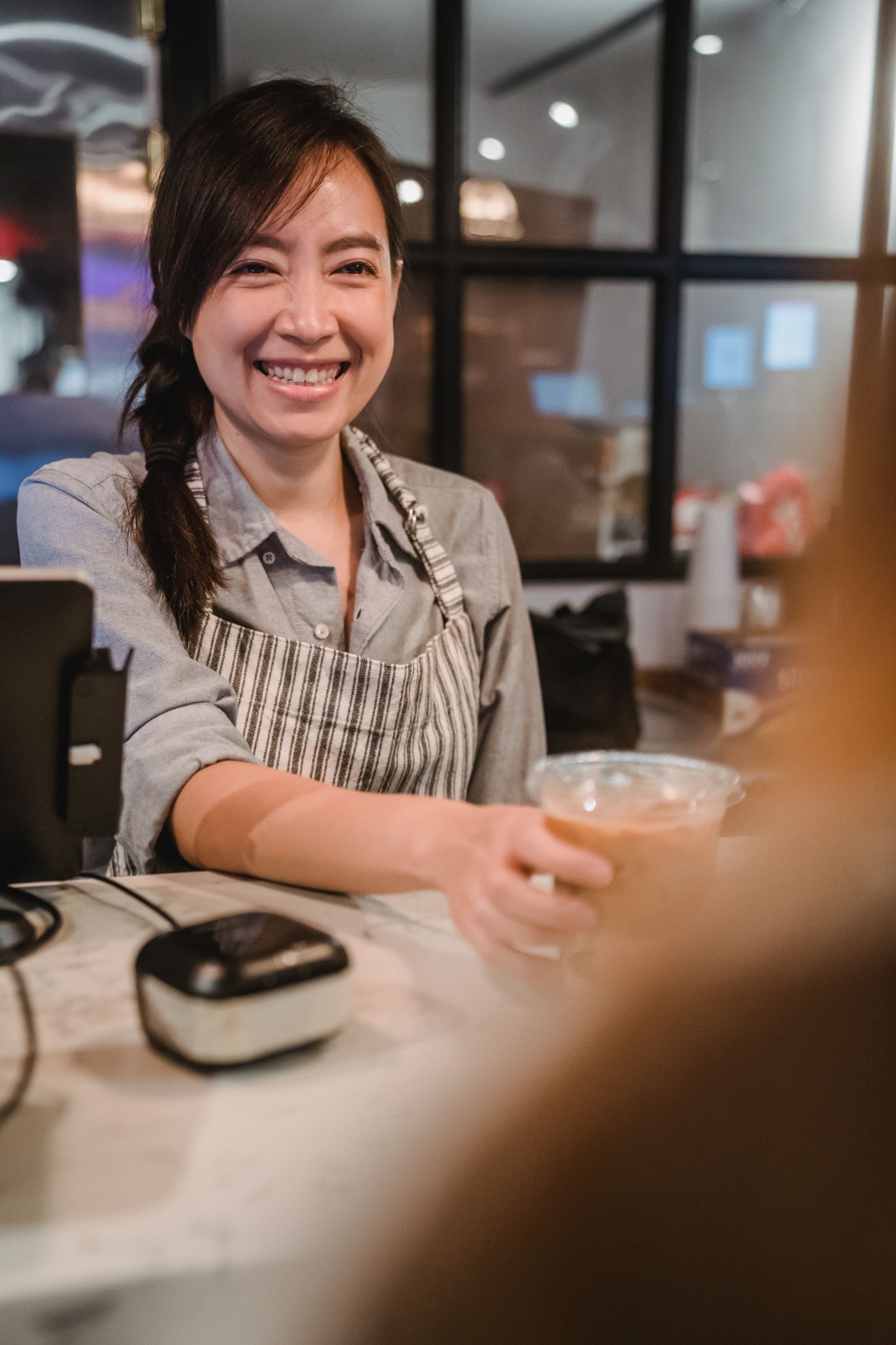 Smiling barista serving coffee at a modern cafe counter.