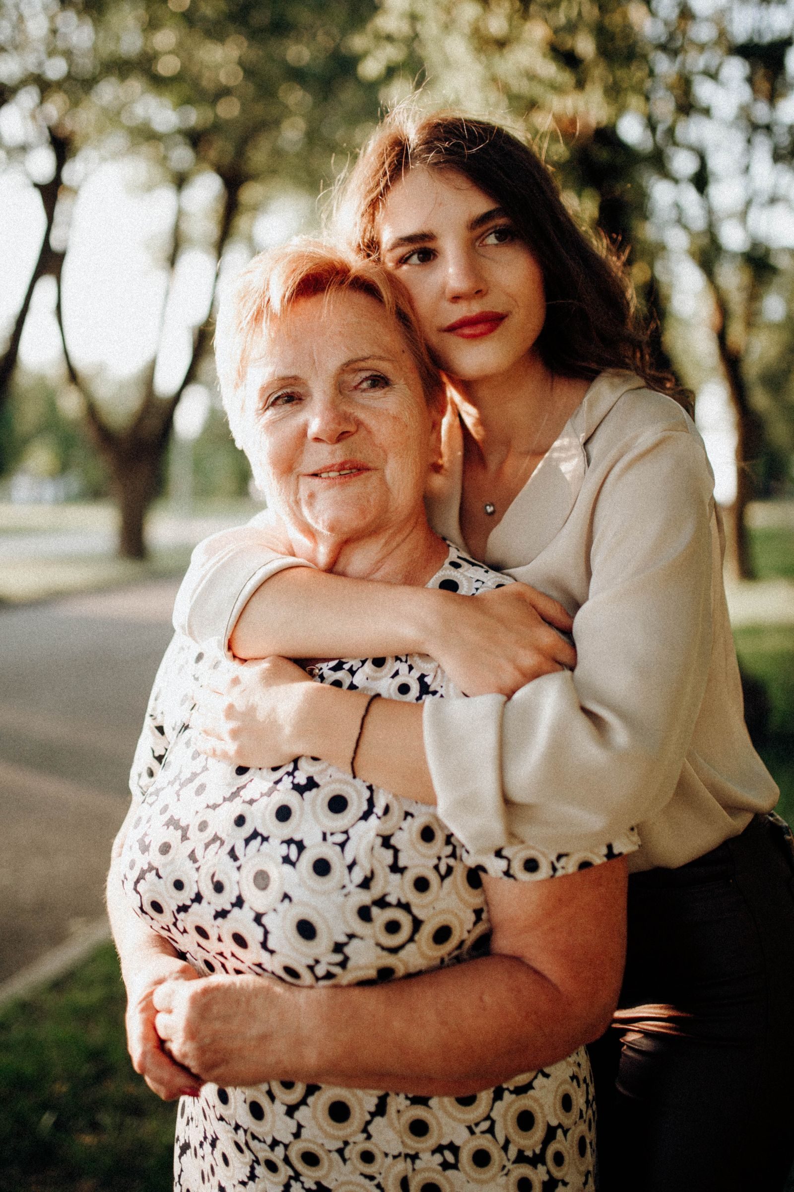 A touching moment between a mother and daughter embracing in a sunlit park setting.