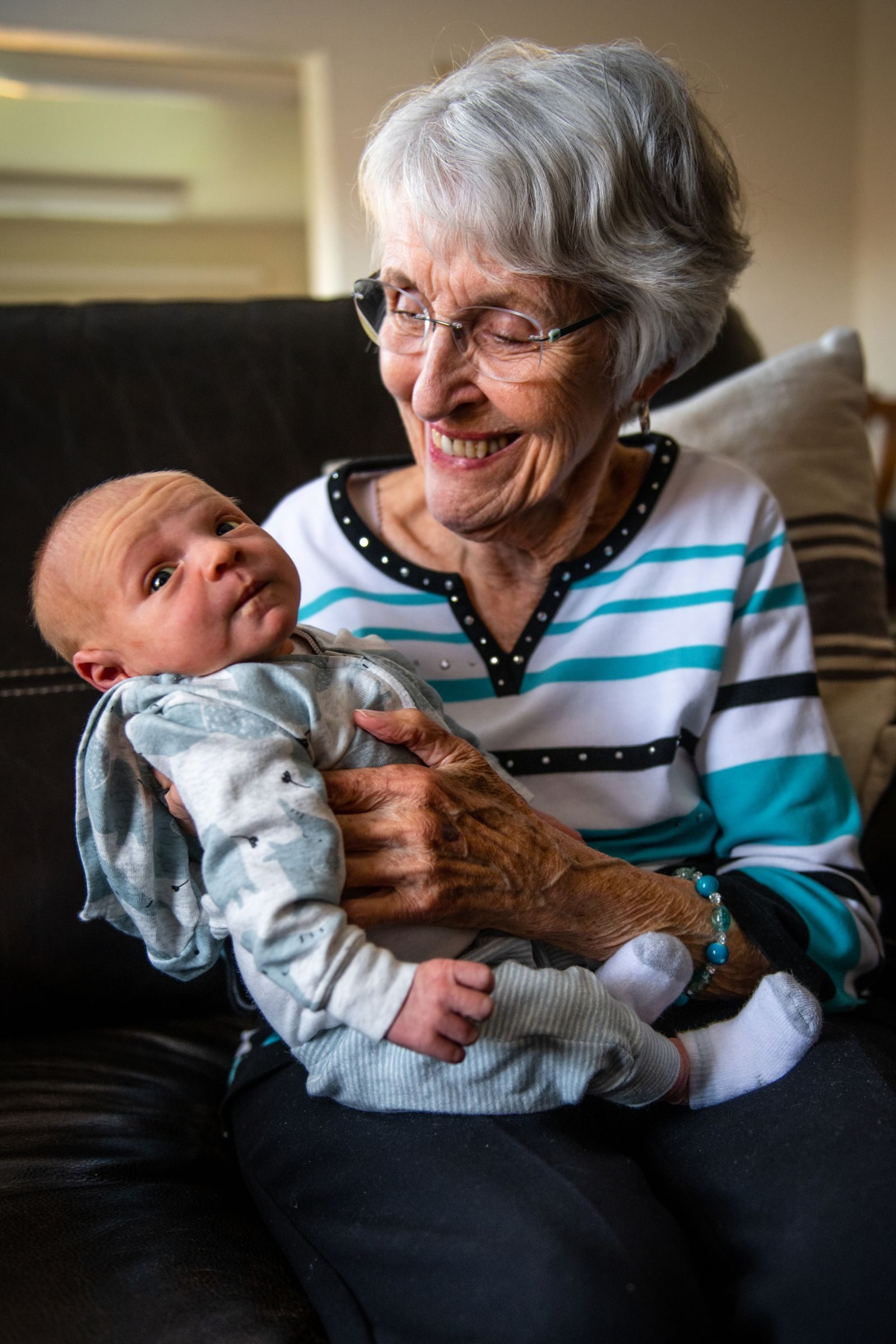 A senior woman lovingly holds her newborn grandchild indoors, conveying warmth and family bonds.