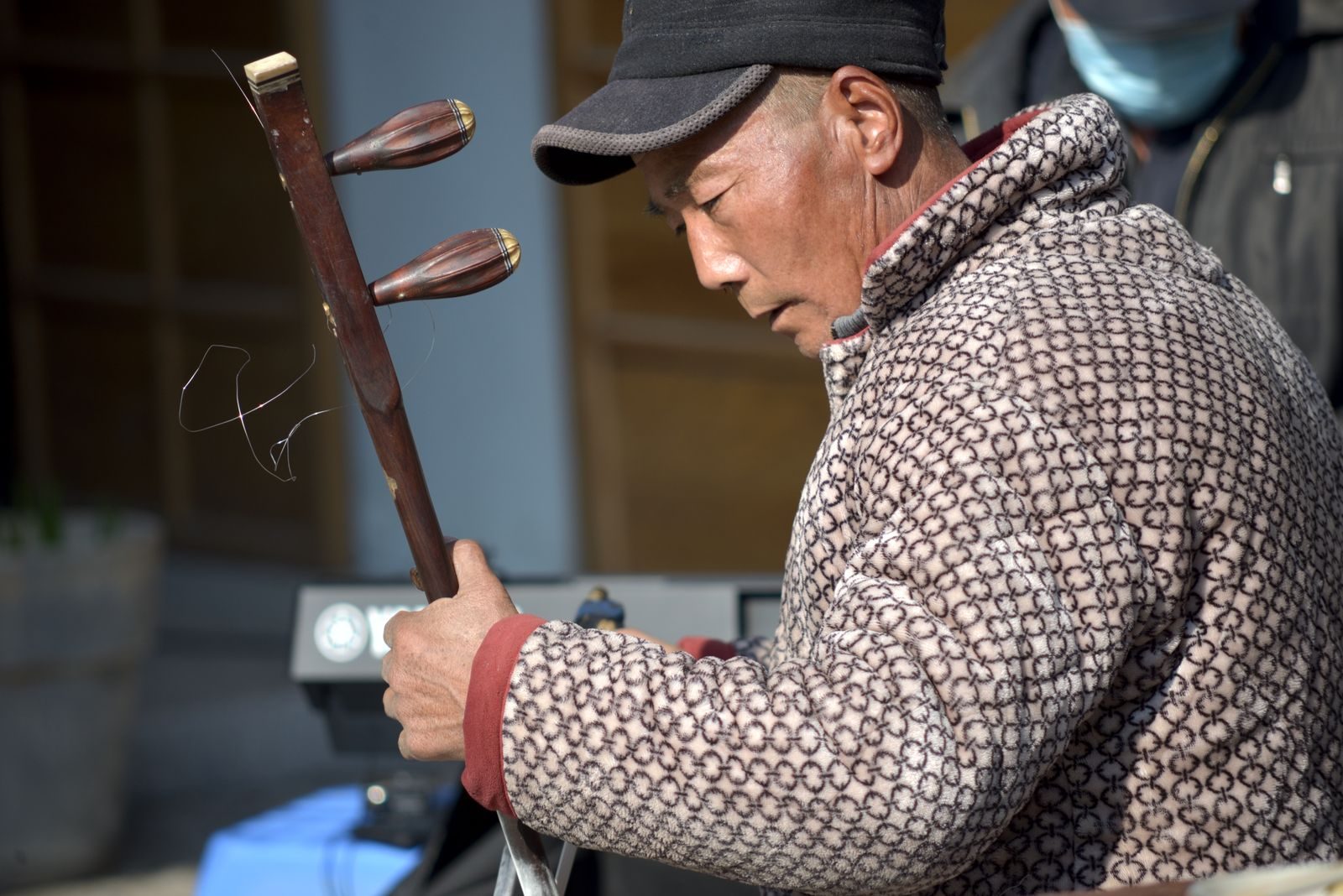 Close-up of a man playing the Chinese erhu outdoors, showcasing cultural music traditions.