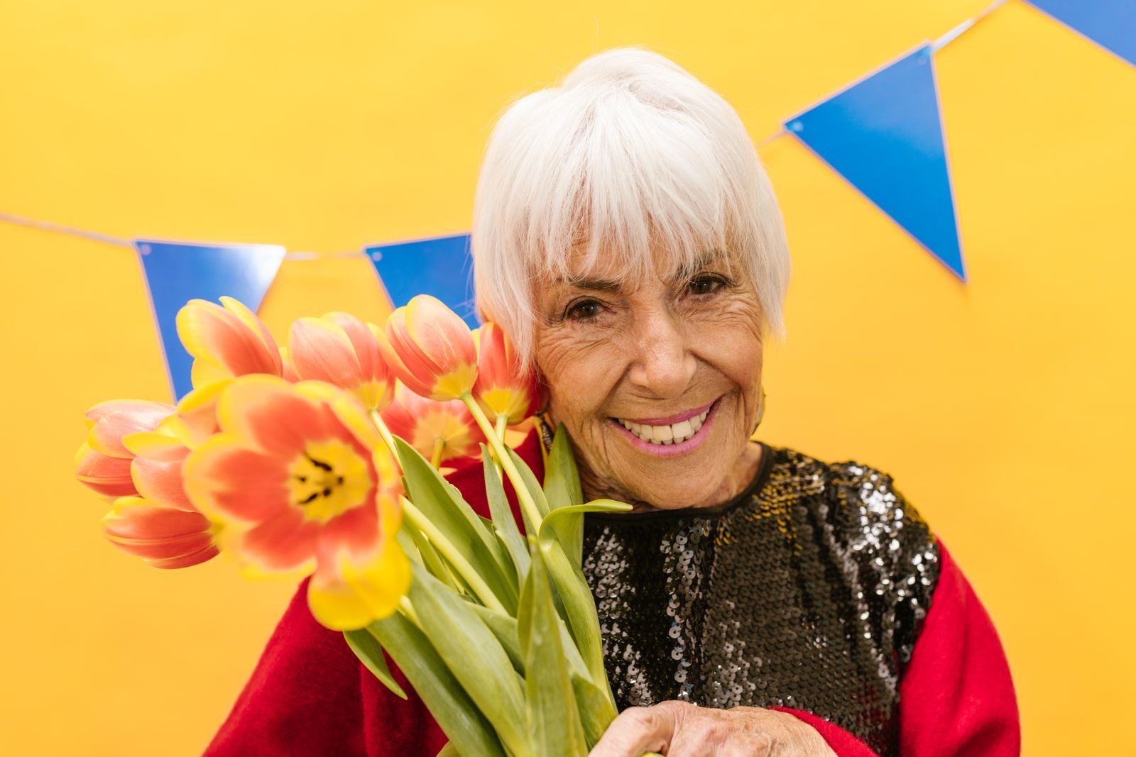 A joyful senior woman smiling while holding vibrant tulips against a festive backdrop.
