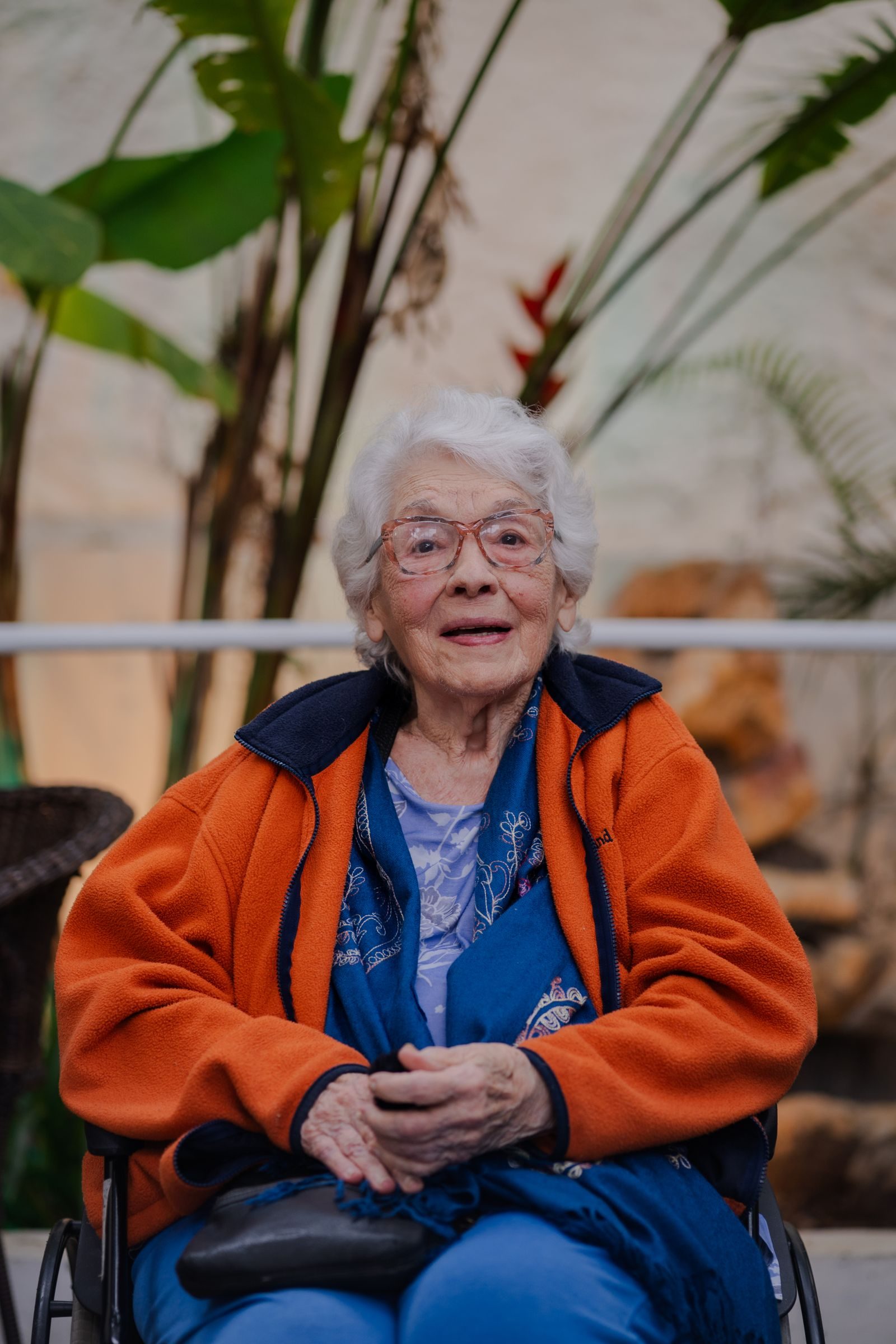 Elderly woman in a wheelchair with plants in the background.
