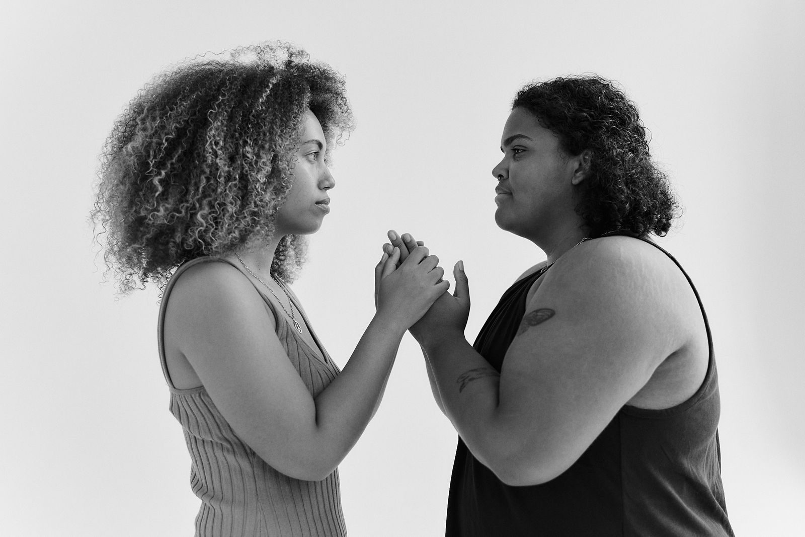Black and white image of two women facing each other, holding hands, symbolizing unity and connection.
