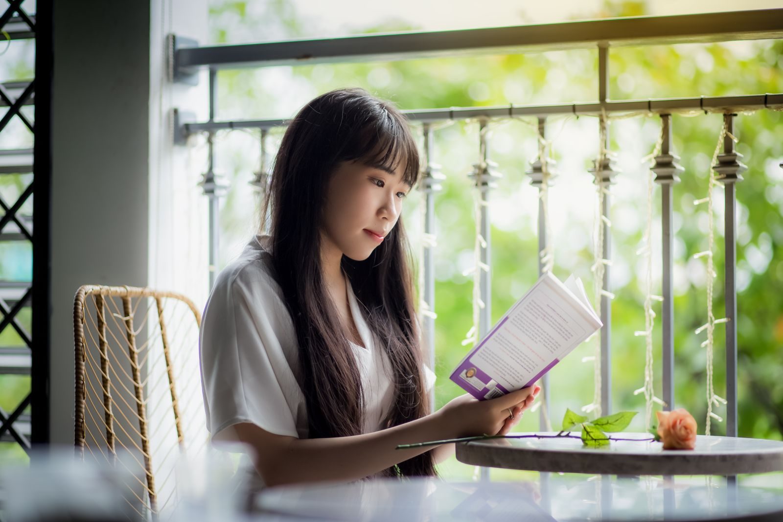 A serene portrait of a woman reading a book on a sunny balcony, surrounded by greenery.