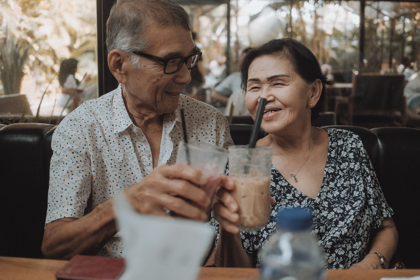 Happy senior couple sharing a moment with iced beverages in a cozy cafe setting.
