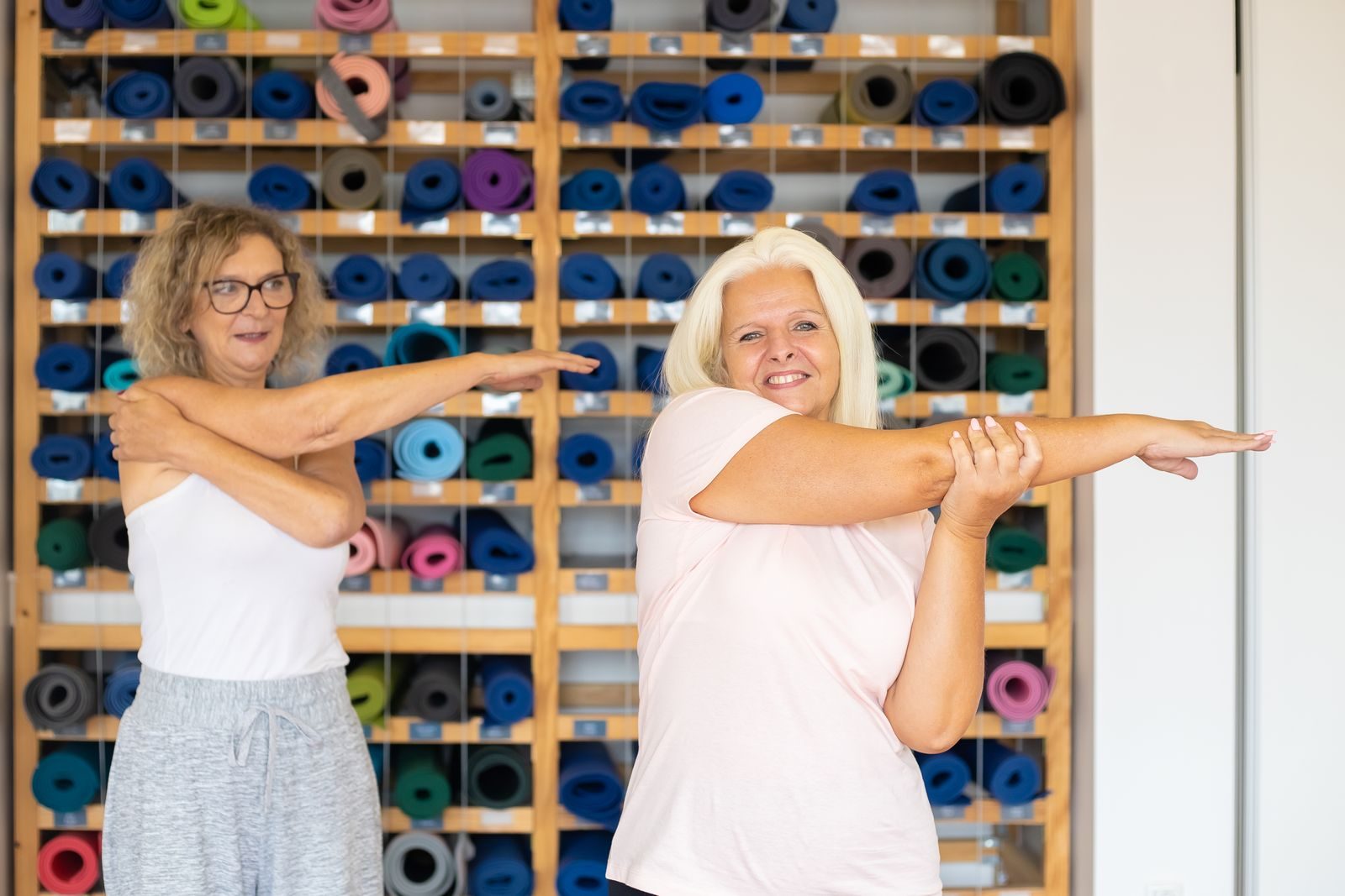 Two women doing arm stretches in a vibrant yoga studio, promoting fitness and wellness.