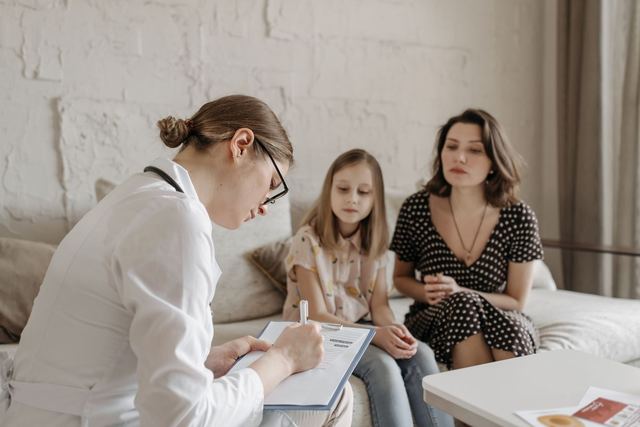 A female doctor consults with a mother and daughter inside a cozy room.