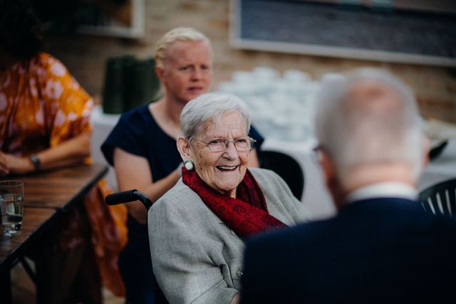 Smiling elderly woman enjoying company at an outdoor gathering, exhibiting warmth and happiness.