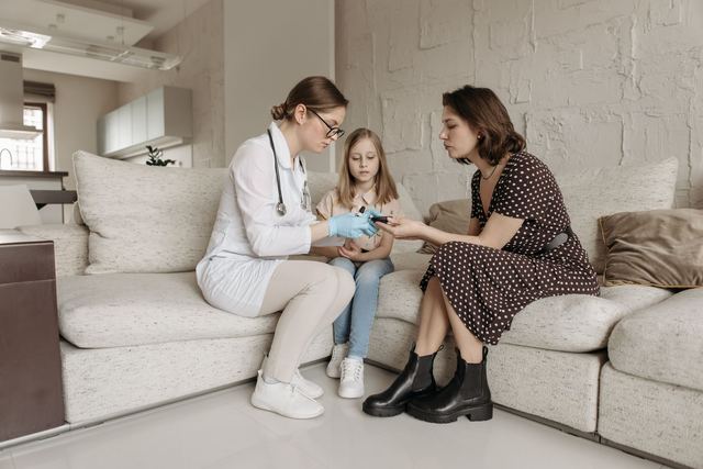 A medical professional examines a child's hand while the mother watches closely.