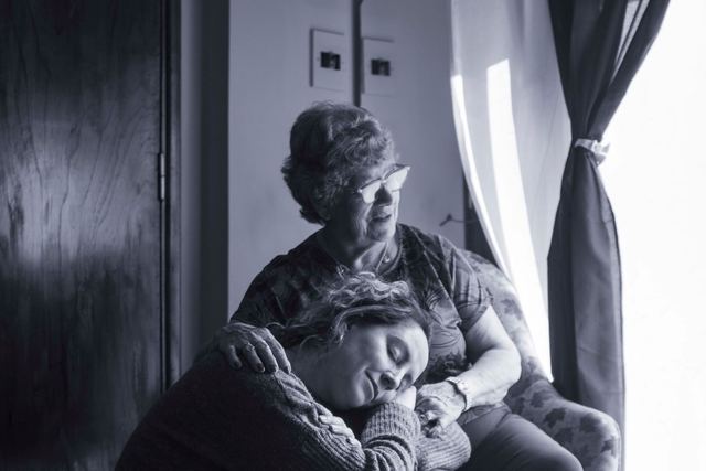 Touching scene of a woman resting her head on her elderly mother's knee, showcasing love and connection.