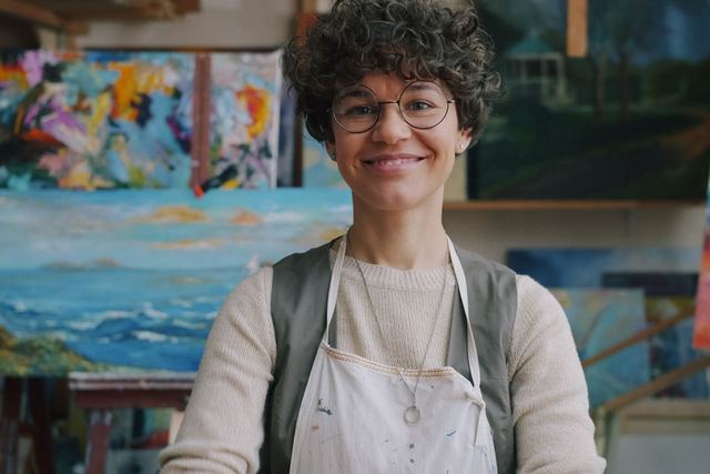 Artist in studio with vibrant paintings around, radiating creativity and joy.