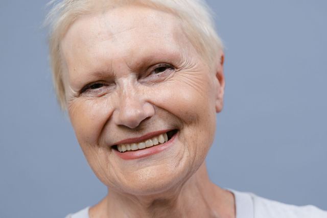 Close-up portrait of a smiling elderly woman against a blue background.