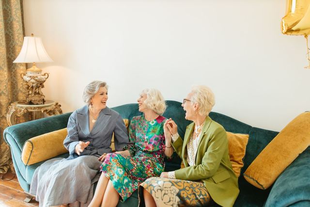 Three elderly women sharing laughter and friendship on a cozy couch indoors.