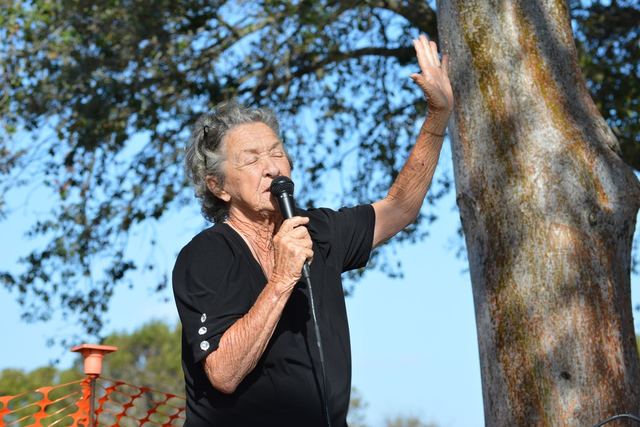 Senior woman enjoying outdoor singing event, eyes closed in performance.
