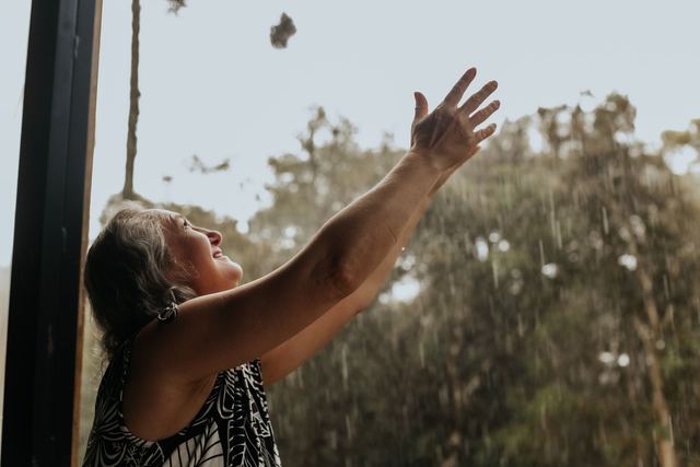 Smiling woman with arms raised, feeling the rain outdoors. Captures freedom and joy.