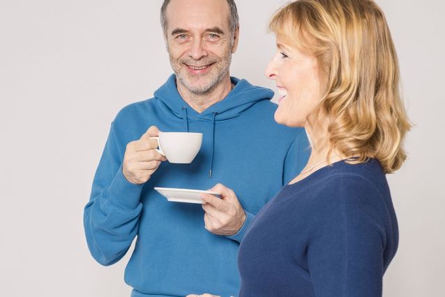 Smiling senior couple sitting indoors enjoying tea. Both appear happy and relaxed.