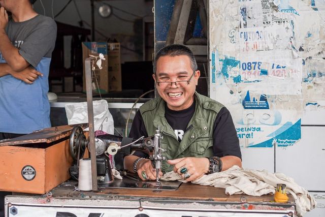 Smiling tailor working on vintage sewing machine in street market, capturing local craftsmanship and joy.