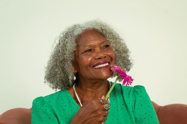 Portrait of a joyful elderly woman in green with a pink flower, exuding happiness.