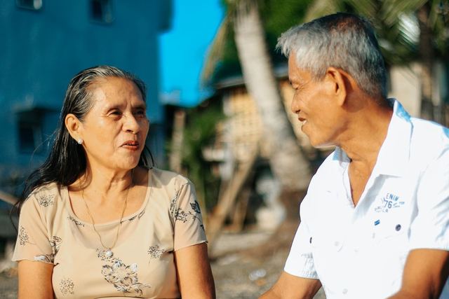 Elderly couple sitting outside, sharing a joyful moment together in a sunny setting.
