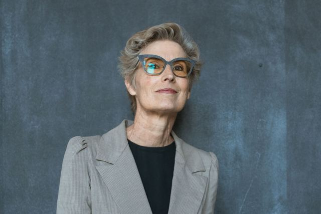 Sophisticated adult woman in glasses with gray coat, smiling while writing in a notebook.