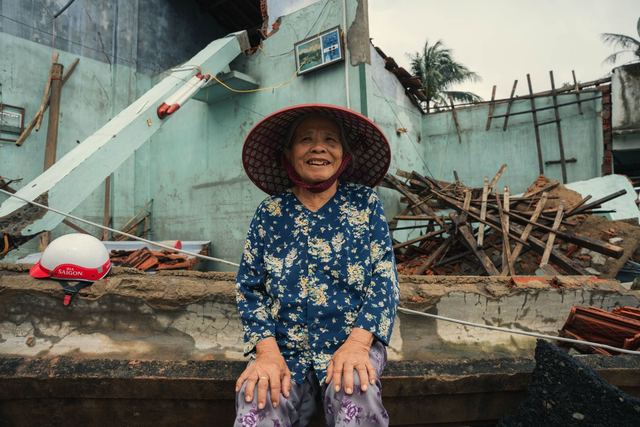 An elderly woman sits smiling in front of building ruins in Phú Yên, Vietnam.