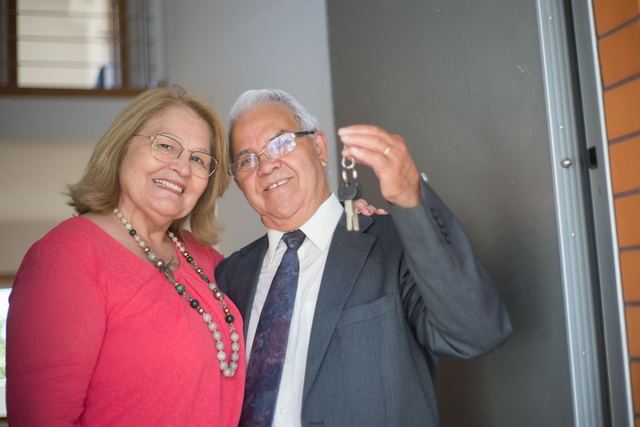 Elderly couple happily holding keys, symbolizing new homeownership.