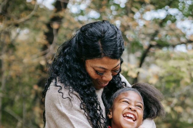 African American woman embracing gently cheerful girl in casual wear in countryside in daytime
