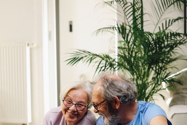Elderly couple sitting on yoga mats, smiling with green smoothies, promoting healthy living.