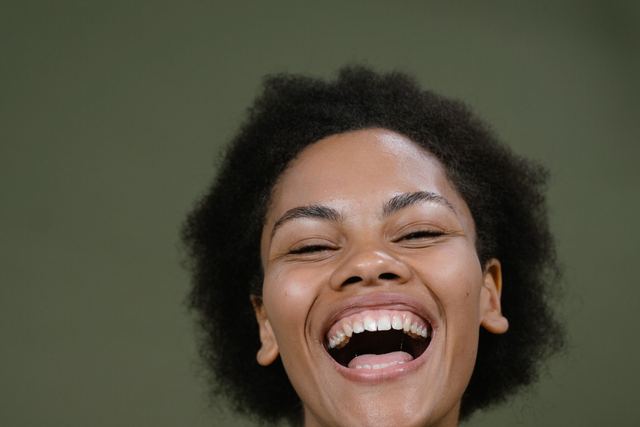 A vibrant woman laughing heartily in a studio with a green backdrop, exuding happiness.