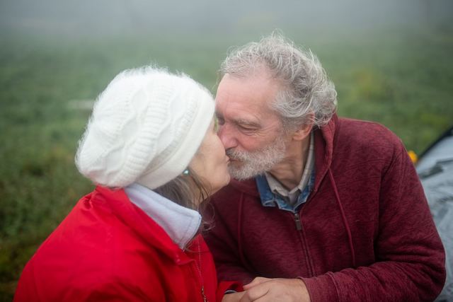 Senior couple sharing a loving kiss outdoors on a foggy day, capturing affection and connection.