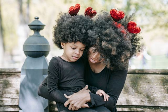 A mother and daughter with heart decorations share a loving embrace outdoors.