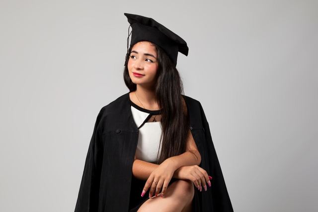 Portrait of a woman wearing a graduation gown and mortarboard, seated confidently in a studio.
